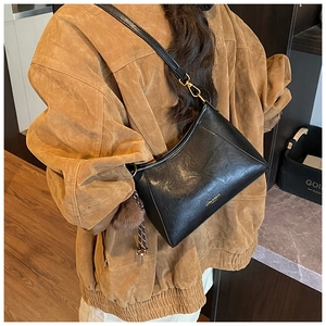 Detail der schwarzen Achseltasche aus Kunstleder mit Goldlogo und braunem Bommel