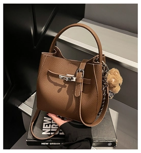 Close-up of brown litchi grain leather bucket bag with metal buckle and teddy bear charm