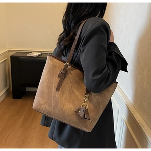 Close-up of tan suede tote bag with delicate elephant charm and gold foil branding