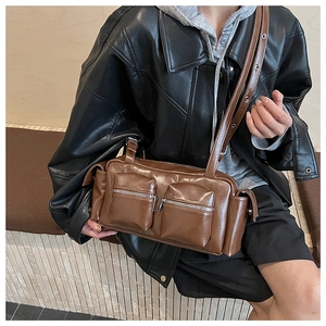 Detail view of the brown glossy faux leather multi-pocket baguette bag worn by a model