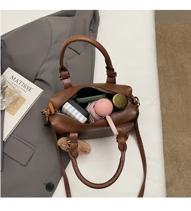 Detailed shot of a brown leather Boston bag with plush ball charm on a white sheet