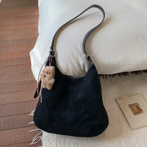 Detail of black suede tote bag with adjustable strap and brown plush bear charm