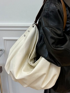 Retro off-white canvas tote bag with brown leather strap worn by a model in a side view