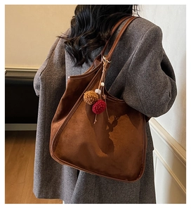 Détail d'un sac hobo en daim marron foncé avec pompons porté sur un blazer en laine