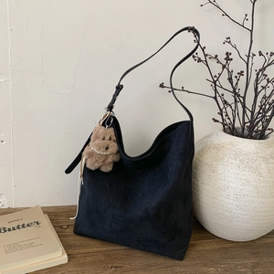 Détail du sac hobo en daim noir avec breloque ours en peluche sur table en bois