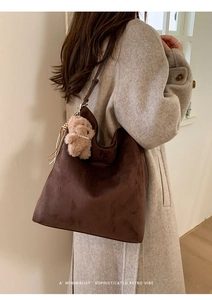 Détail d'un sac hobo en daim marron foncé avec un charmant petit ours sur le côté