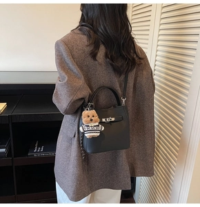 Detail of black lychee texture bucket bag with silver lock and teddy bear charm accessory