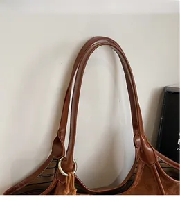 Détail de la bandoulière en cuir marron avec anneau doré et doublure rayée du sac