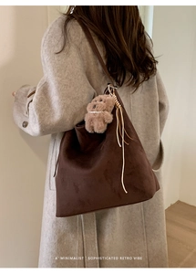 Détail du sac hobo en daim marron foncé avec pendentif ours sur un manteau gris