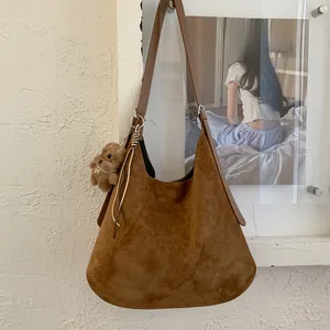 Detailed view of brown suede hobo bag with plush bear charm and tassel decoration