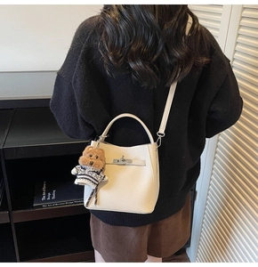 Off-white leather bucket bag with a teddy bear charm shown on a shoulder