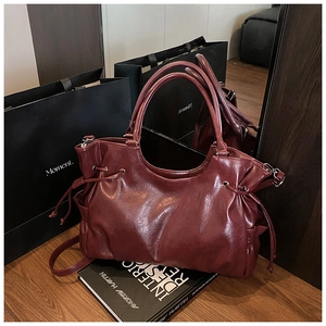 Detail of burgundy faux leather tote bag with drawstring closure on wooden display
