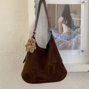 Close-up of brown faux suede tote bag with a cute plush bear charm on white textured wall