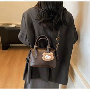 Detail of vintage brown leather boston bag with adjustable shoulder strap and plush bear charm