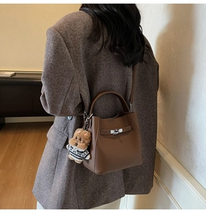 Brown lychee leather bucket bag featuring a silver metal turn-lock and a cute bear charm