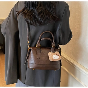 Detail view of dark brown retro pillow bag with round handles and plush bear charm