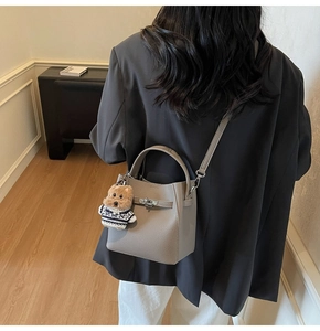 Detail view of a grey bucket bag with metal buckle and cute teddy bear charm on strap