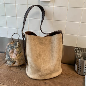Détail du sac seau en daim kaki avec bandoulière en cuir tressé marron foncé