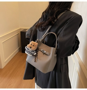 Close-up of a grey litchi leather bucket bag featuring a rotating lock and plush dog charm