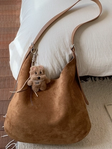 Brown faux suede tote bag with plush charm and long shoulder straps in cozy setting