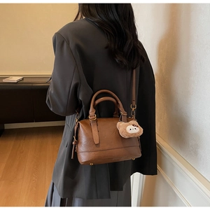 Side view of dark brown retro Boston bag with plush bear charm on a female model