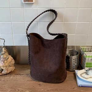 Détail du sac seau en cuir mat chocolat avec bandoulière tissée sur une table en bois