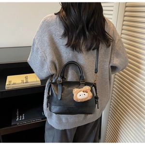 Detail of black leather Boston bag with plush bear charm and gold hardware on model