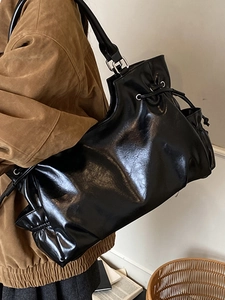 Glossy black drawstring shoulder bag in faux leather with a minimalist pleated design