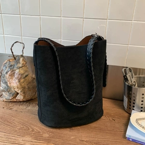 Détail du sac seau en daim noir avec bandoulière tissée et boucle en métal sur bois