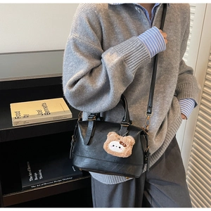 Detail view of black leather crossbody bag with a cute brown plush bear charm accessory