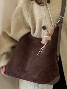 Brown suede hobo tote bag with bear charm worn with beige coat in minimalist fashion