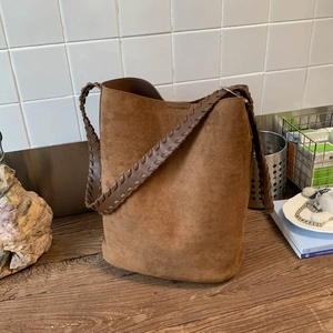 Détail du sac seau en daim marron avec bandoulière tissée au design sophistiqué