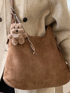 Brown suede tote bag with plush dog pendant shown on a beige wool coat outfit