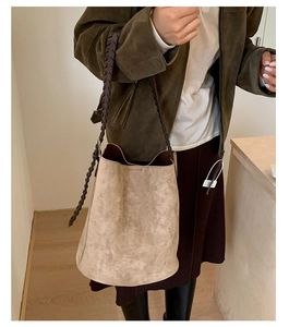 Détail du sac seau beige avec bandoulière en cuir tressé marron foncé et texture lisse