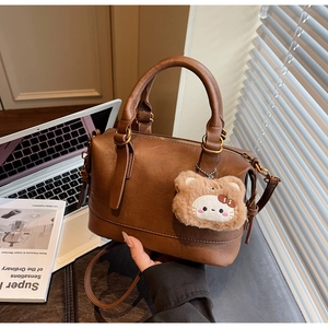 Brown lychee leather Boston bag with plush charm on a desk with laptop and magazine