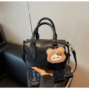 Close-up of black Boston handbag featuring dual handles and a cute brown bear charm