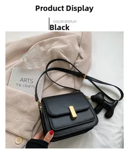 Détail du sac bandoulière en cuir noir avec boucle dorée et accessoire de charme chiot