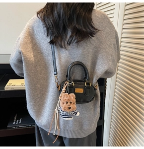Dettaglio della mini borsa Boston in pelle nera con ciondolo teddy su maglione grigio