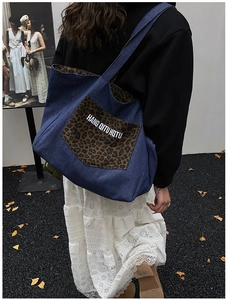 Deep blue denim tote bag with leopard print pocket shown in a lifestyle street setting