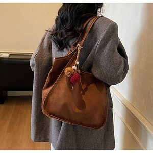 Détail du sac fourre-tout en daim marron avec pompons sur un manteau en laine gris