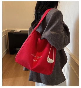 Détail du grand sac cabas en toile rouge avec lettrage blanc sur un blazer gris élégant