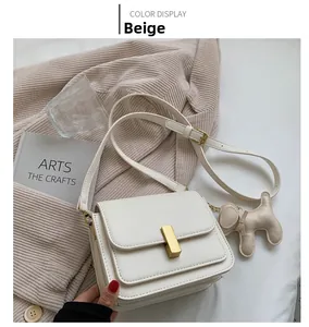 Détail du sac bandoulière en cuir beige avec fermoir doré et breloque chien sur tricot