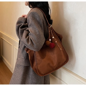Vue détaillée du cabas en daim marron avec pompons en peluche et bandoulière en cuir