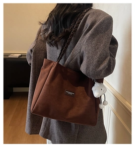 Detail of a brown suede tote bag with woven handles and white cloud plush charm