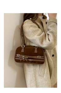 Detail of dark brown suede ballet-style bowling bag with bow and buckle on a model shoulder