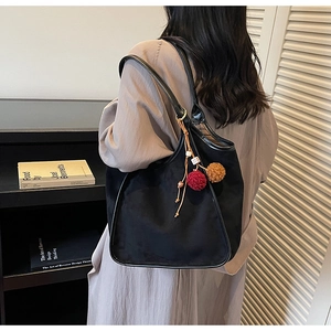 Détail du sac cabas en daim noir avec pompons colorés et bandoulière en cuir souple