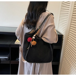 Détail d'un sac cabas en daim noir avec pompons en peluche et fines anses en cuir