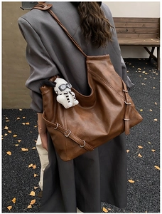 Detail view of large brown leather tote bag with silver eyelet straps and plush dog charm