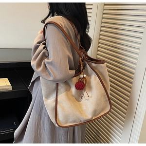 Détail du sac cabas en toile avec garniture en cuir brun et breloque porté par un mannequin