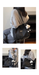 Detail of black canvas tote bag featuring braided leather strap and plush white charm